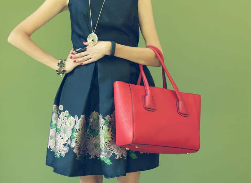 fashionable beautiful big red handbag on the arm of the girl in a fashionable black dress, posing near the wall on a warm summer night. warm color